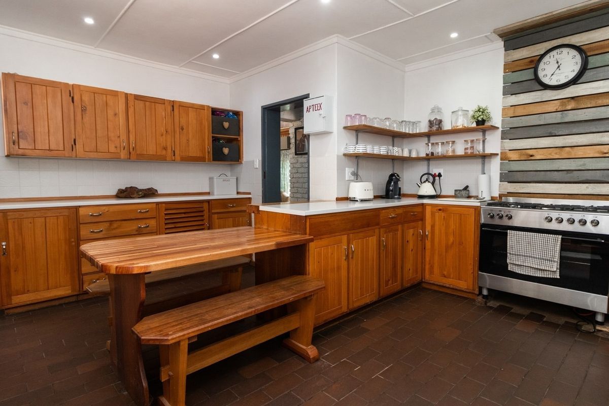 A rustic-style kitchen featuring wooden cabinetry, open shelving, a built-in oven with gas hob, and durable tiled flooring.