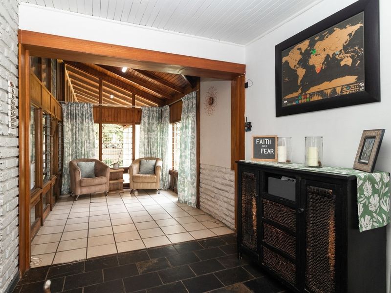 Spacious living area featuring exposed timber ceiling beams, a brick feature wall, and large windows that provide ample natural light.
