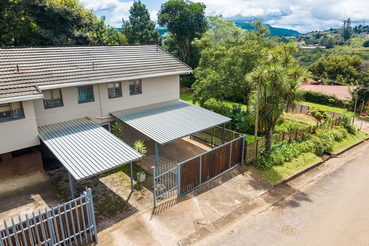 Aerial view of the property featuring a double carport, paved driveway, secure perimeter fencing, and a tiled roof structure.