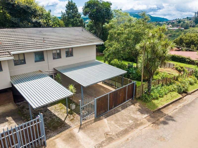 Aerial view of the property featuring a double carport, paved driveway, secure perimeter fencing, and a tiled roof structure.