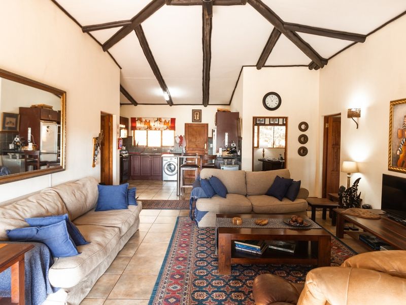 Spacious open-plan living area featuring exposed timber ceiling beams, tiled flooring, and a connected kitchen space with built-in cabinetry.