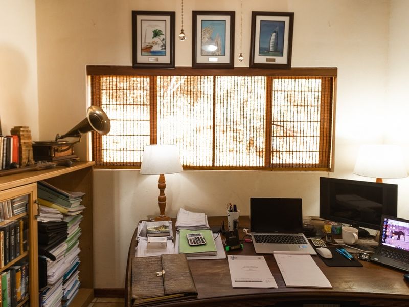 A functional home office space featuring a built-in wooden shelving unit and a window with integrated bamboo-style blinds.
