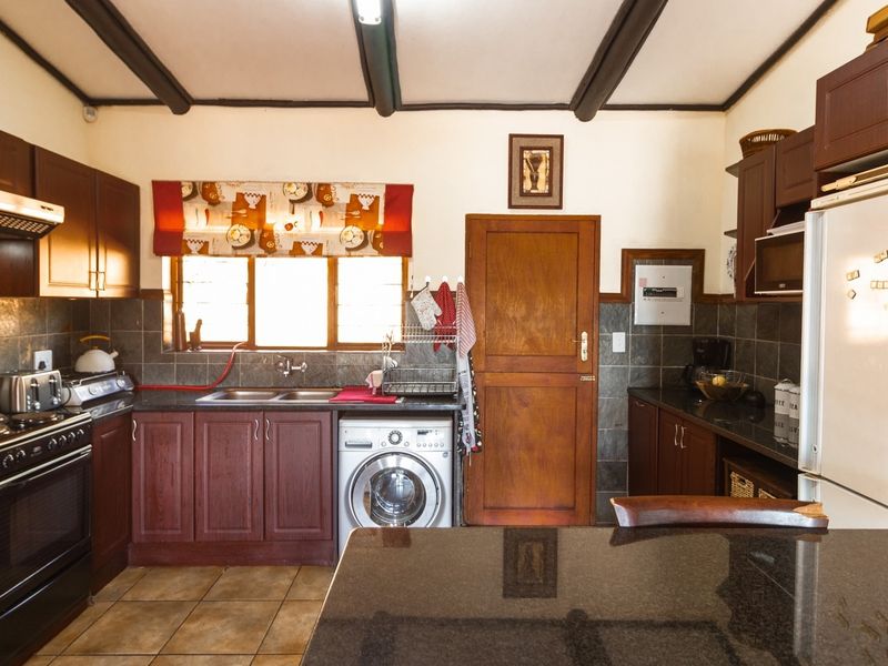 A functional kitchen featuring dark wood cabinetry, granite countertops, a double basin sink, built-in oven, and exposed ceiling beams.