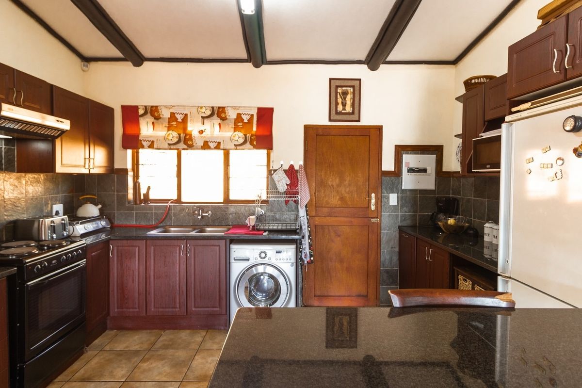 A functional kitchen featuring dark wood cabinetry, granite countertops, a double basin sink, built-in oven, and exposed ceiling beams.