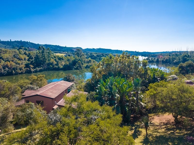Aerial view of a residential property nestled in a lush, green landscape with direct access to a scenic river or lake.