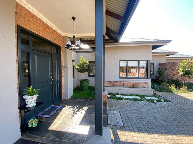A well-maintained covered entrance featuring a brick facade, tiled patio, and a built-in brick planter box, leading to a modern front door.