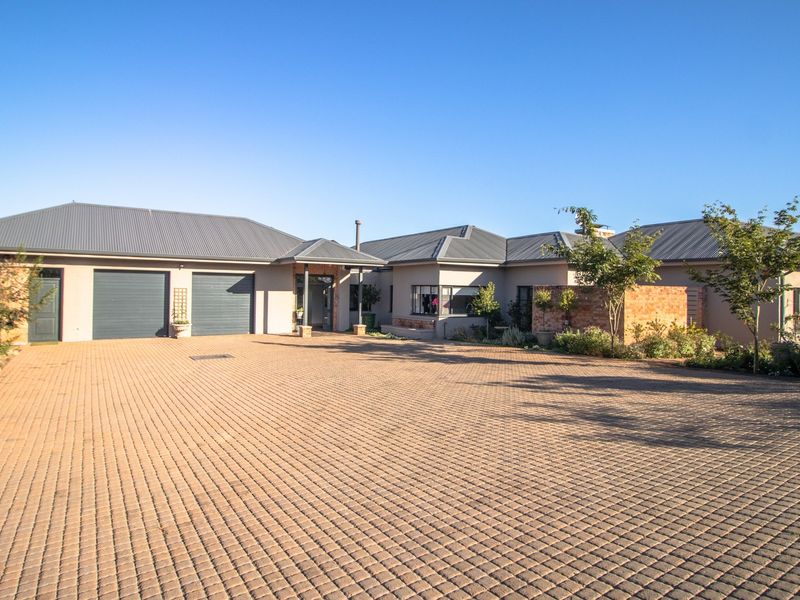 A well-maintained single-story house featuring a spacious paved driveway, double garage, and a covered entrance with a modern metal roof.