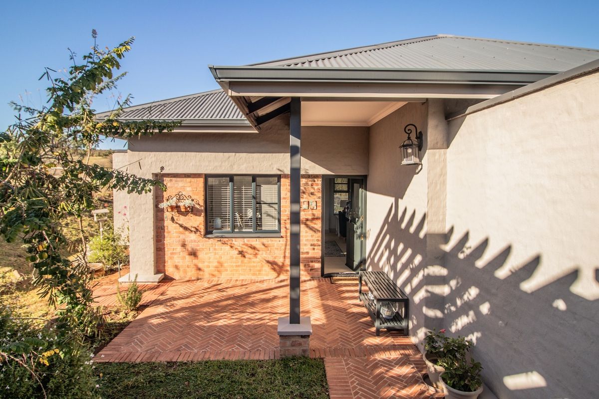 A well-maintained rear exterior featuring a covered veranda with brick paving, exposed brick accents, and a modern metal roof.