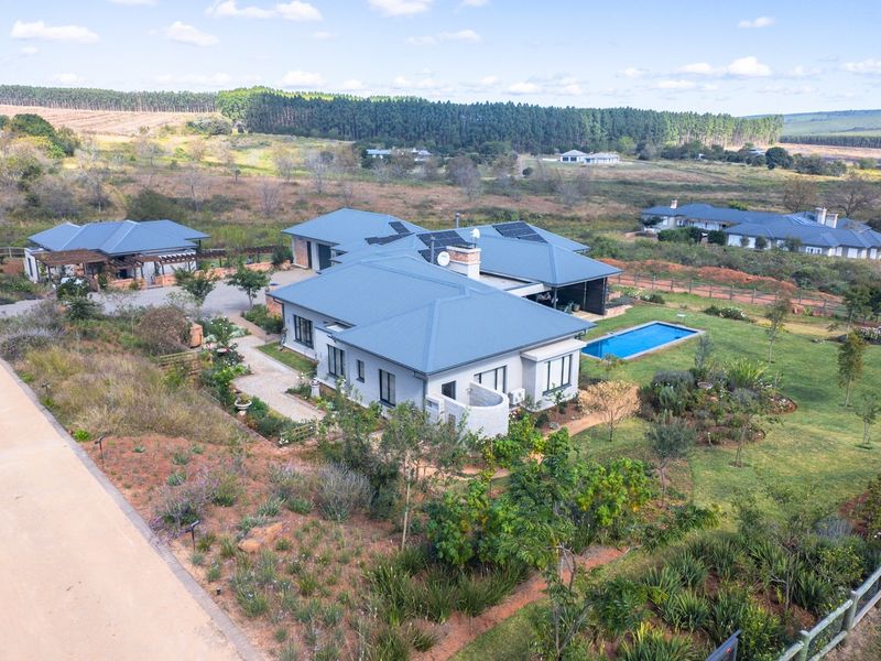 Aerial view of a spacious residential property featuring a main house, swimming pool, landscaped gardens, and a long paved driveway in a rural setting.