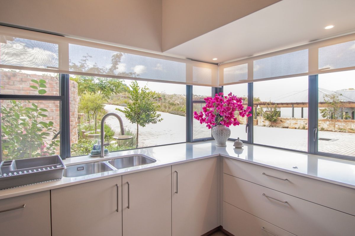 Modern kitchen featuring sleek cabinetry, quartz countertops, and a double sink, with large corner windows providing ample natural light and garden views.
