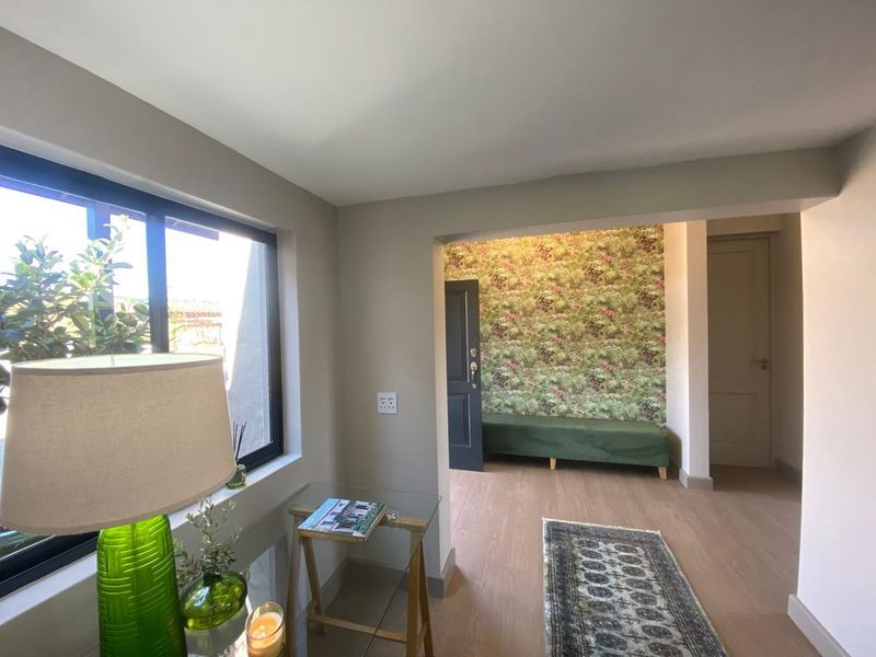 A bright living area featuring modern laminate flooring, neutral wall tones, and large aluminium-framed windows providing natural light.