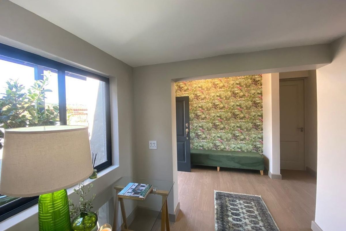 A bright living area featuring modern laminate flooring, neutral wall tones, and large aluminium-framed windows providing natural light.