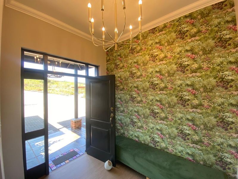 Welcoming entrance hall featuring a statement chandelier, decorative floral wallpaper, and a solid timber front door opening to an outdoor patio area.
