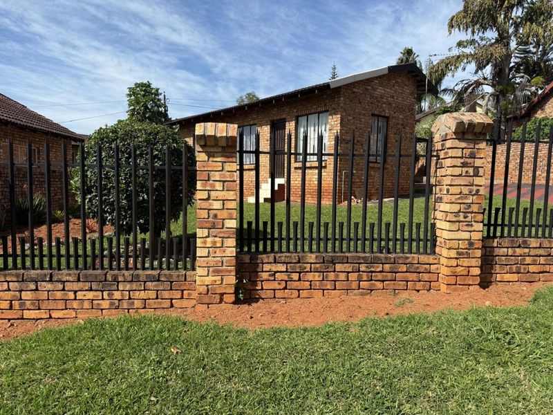 Front view of a face brick house featuring a secure metal fence with brick pillars and a well-maintained lawn.