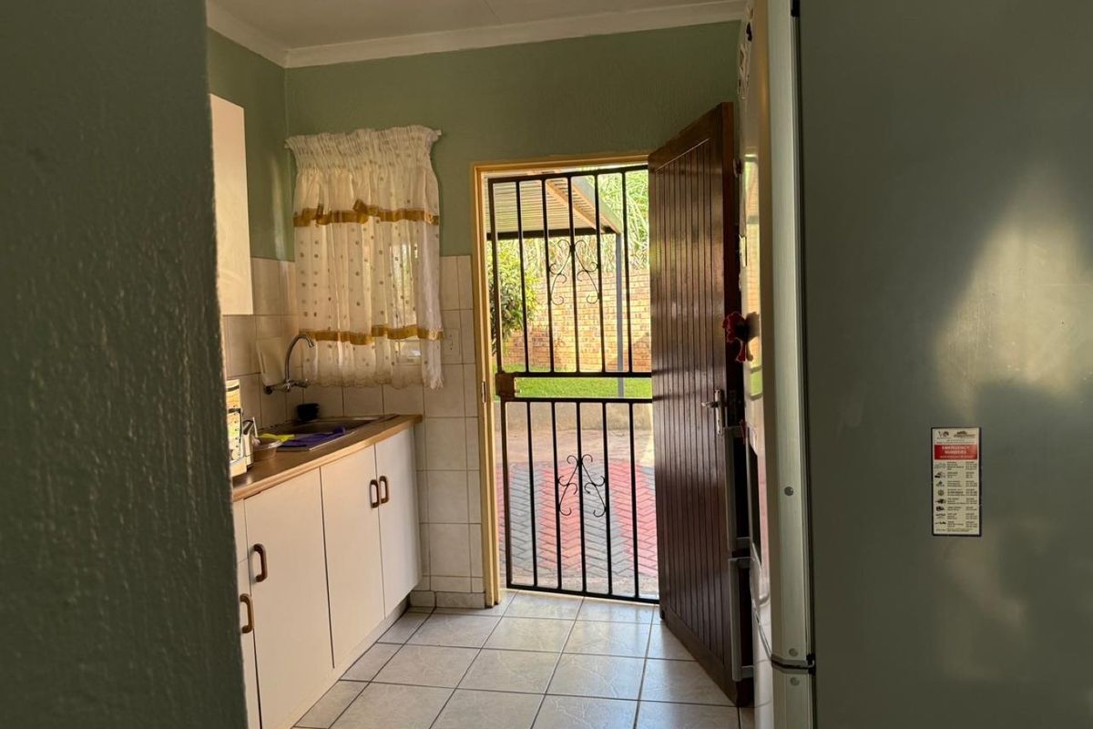 A functional kitchen area featuring built-in cabinetry, tiled splashbacks, and direct access to the exterior through a secure gate and timber door.