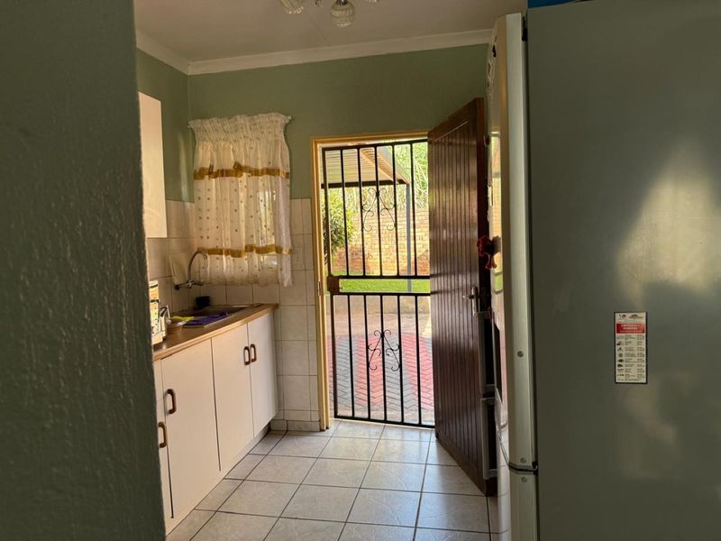 A functional kitchen area featuring built-in cabinetry, tiled splashbacks, and direct access to the exterior through a secure gate and timber door.