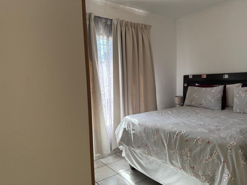 A functional bedroom featuring tiled flooring and natural light through a window with curtain tracks.