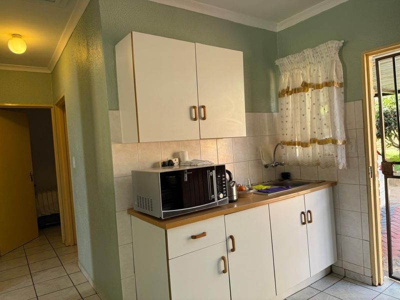 A compact kitchen area featuring white built-in cabinetry, a laminate countertop, stainless steel sink, and tiled backsplash with neutral floor tiles.