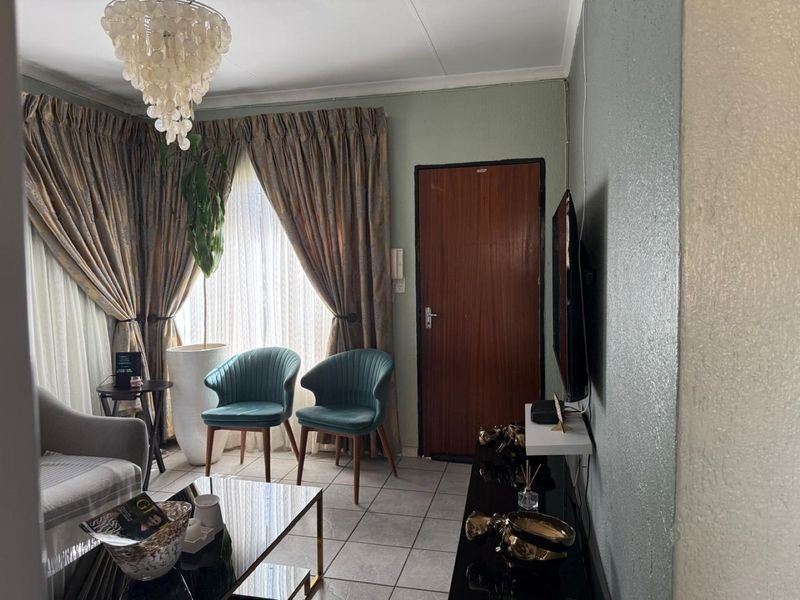 A compact living room featuring tiled flooring, an intercom system, and a central light fixture, providing a functional space for relaxation.