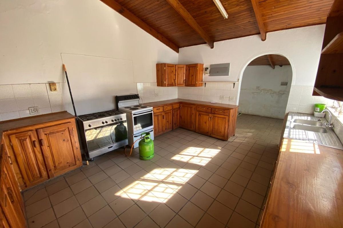 Spacious kitchen featuring wooden cabinetry, tiled flooring, and exposed wooden beam ceilings, leading through an arched doorway to an adjacent utility area.
