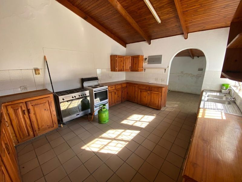Spacious kitchen featuring wooden cabinetry, tiled flooring, and exposed wooden beam ceilings, leading through an arched doorway to an adjacent utility area.