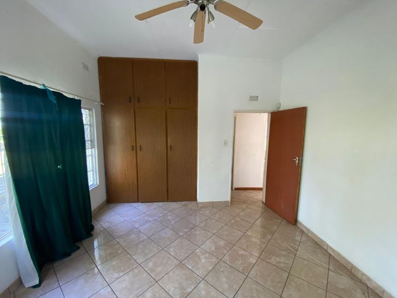 A vacant bedroom featuring tiled flooring, built-in wooden cupboards, and a ceiling fan, offering a clean and functional space ready for personalization.