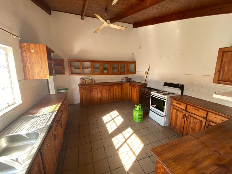 A spacious kitchen featuring wooden cabinetry, tiled flooring, and an exposed timber ceiling, offering a functional layout with potential for modernization.