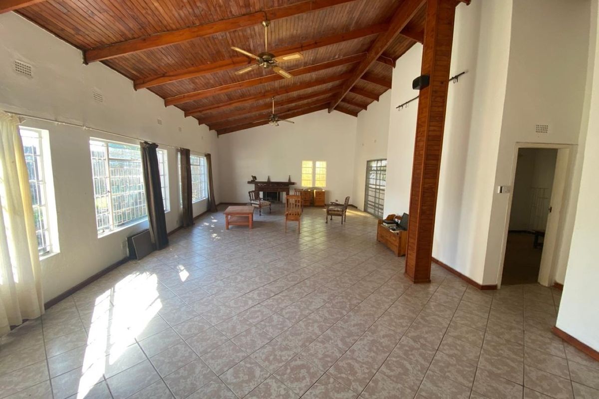 Spacious living area featuring high exposed timber beam ceilings, tiled flooring, and a built-in fireplace, offering a bright and open layout.