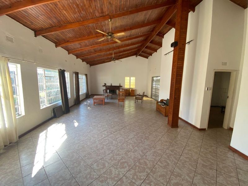 Spacious living area featuring high exposed timber beam ceilings, tiled flooring, and a built-in fireplace, offering a bright and open layout.