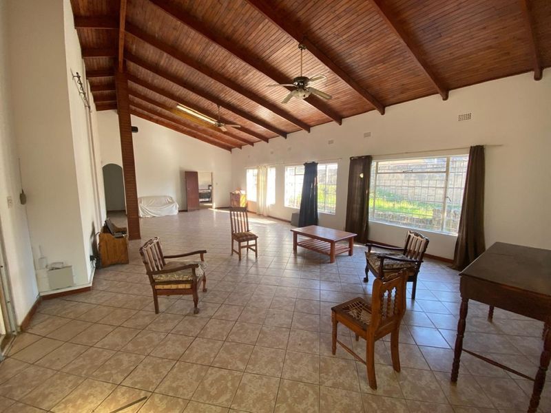 Spacious living area featuring a high vaulted timber ceiling, ceramic tiled flooring, and large windows with security bars, offering a bright and open layout.