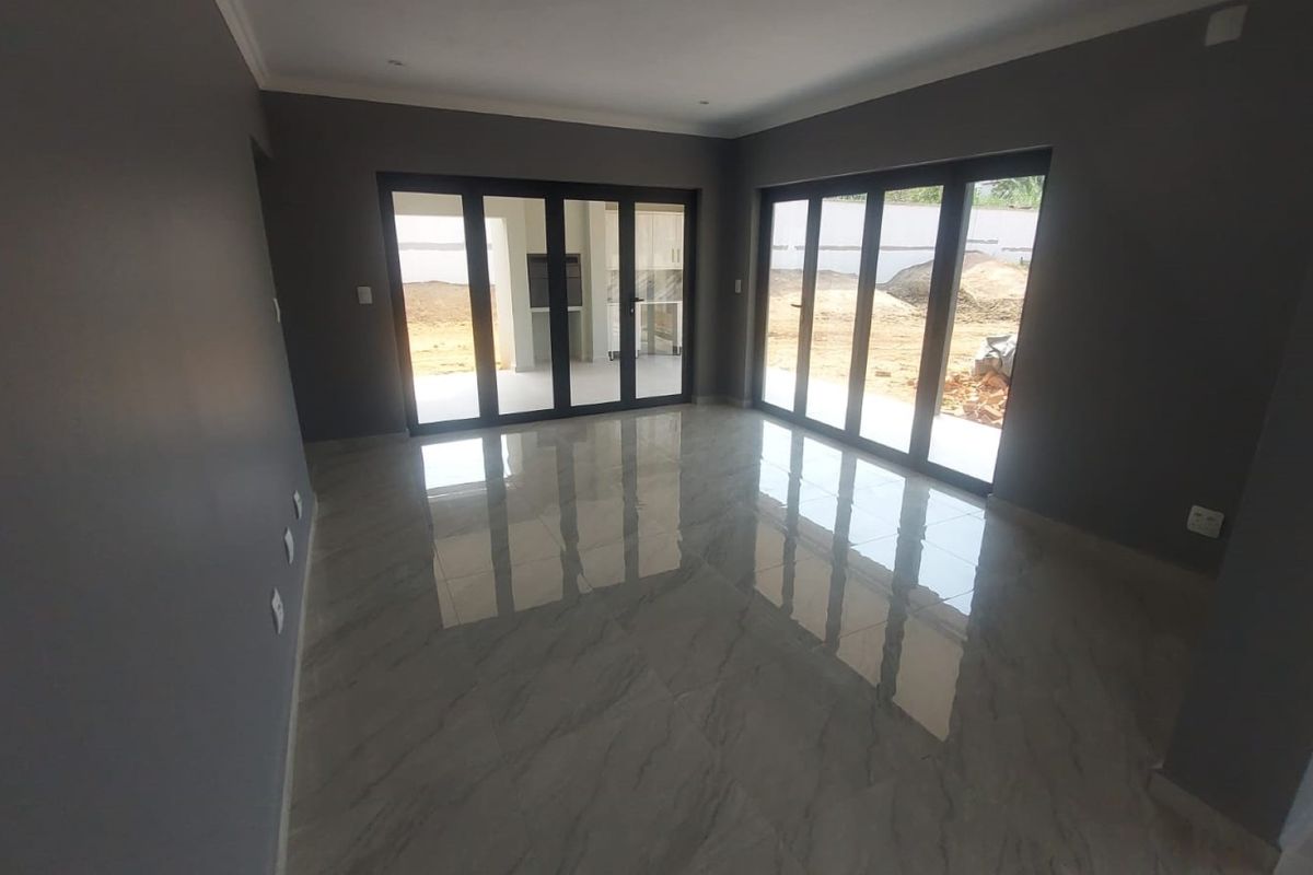 Spacious, modern living area featuring large aluminium stacker doors that open to the exterior, complemented by polished porcelain tiles and neutral grey walls.