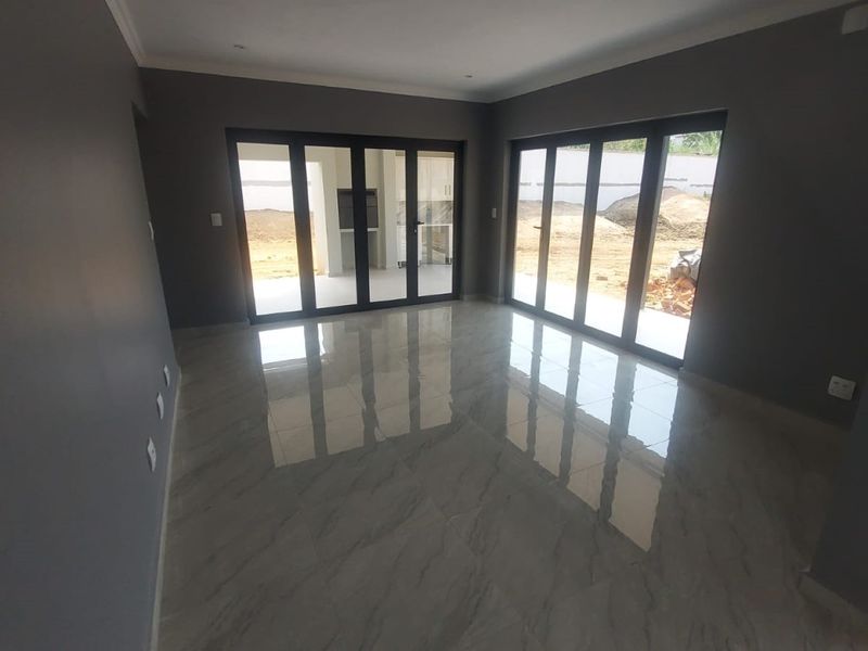 Spacious, modern living area featuring large aluminium stacker doors that open to the exterior, complemented by polished porcelain tiles and neutral grey walls.