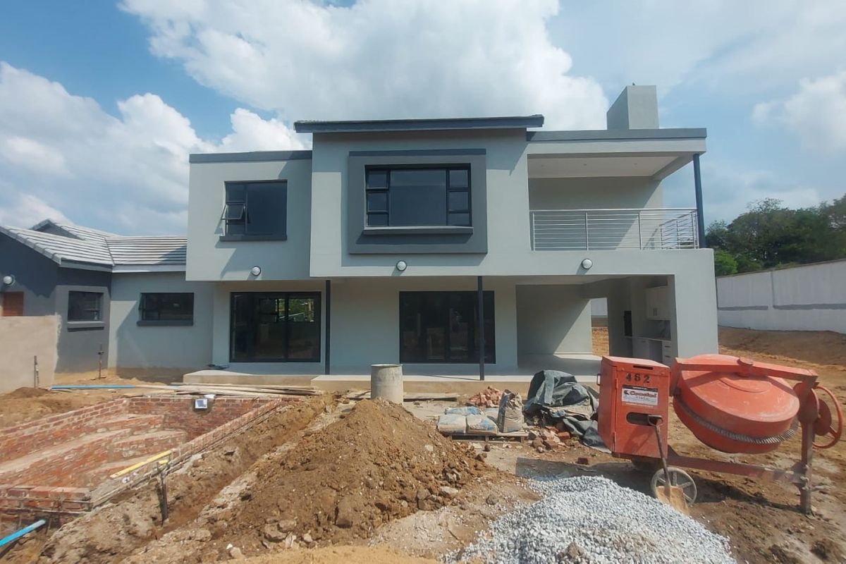 Rear view of a modern double-story townhouse featuring a balcony and patio area, currently undergoing exterior landscaping and site development.