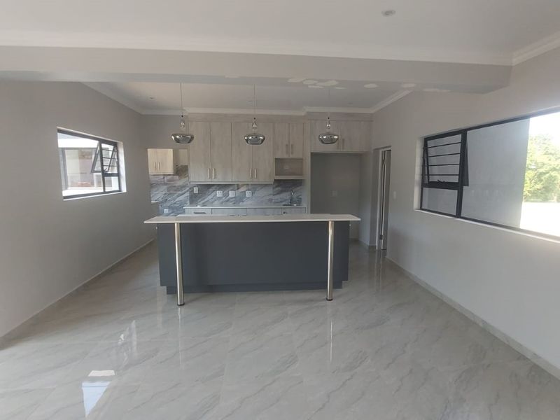 Spacious open-plan kitchen and living area featuring modern cabinetry, a central island, and polished marble-look floor tiles throughout.