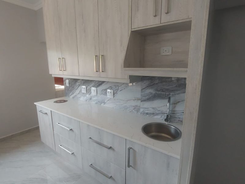 A modern, clean scullery area featuring light wood-grain cabinetry, stone countertops, a marble-look splashback, and a compact stainless steel sink.