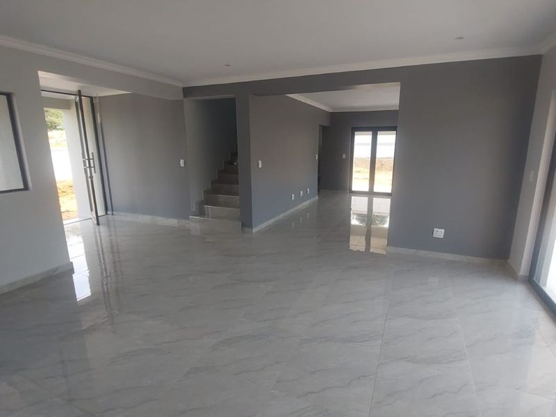 Spacious open-plan living area featuring modern porcelain tile flooring, neutral grey walls, and large sliding glass doors providing ample natural light.