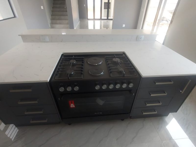 Modern kitchen island featuring a white quartz countertop, integrated gas and electric stove, oven, and dark cabinetry with ample storage space.