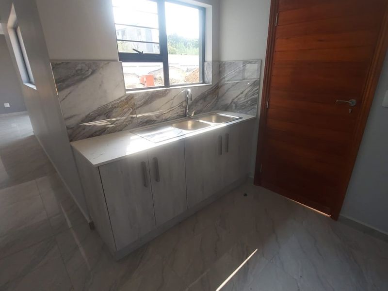 A clean, modern scullery area featuring a double bowl sink, stone countertops, marble-look splashback tiling, and light wood-finish cabinetry.