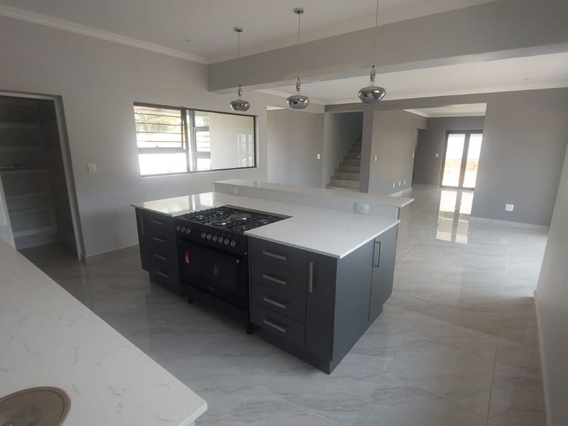 Modern open-plan kitchen and living area featuring a central island with gas hob, stone countertops, and sleek tiled flooring throughout.