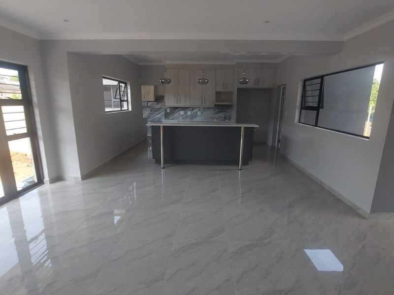 Spacious open-plan living and kitchen area featuring modern cabinetry, a central island, polished marble-look floor tiles, and large sliding doors leading outdoors.