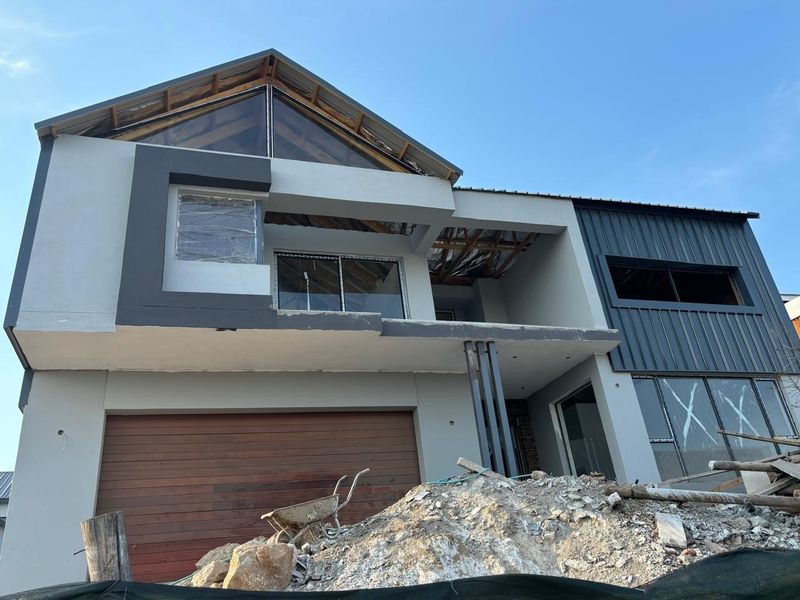 Front elevation of a modern double-storey house currently under construction, featuring a sectional garage door, aluminium window frames, and unfinished roof sections.