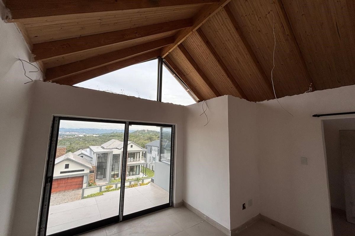 An unfinished bedroom featuring a high vaulted timber ceiling, large sliding glass doors, and expansive views, currently awaiting final wall finishes and electrical fixtures.