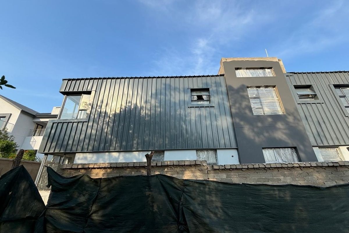 Rear elevation of a modern house featuring corrugated metal cladding and plastered sections, currently in an unfinished state with protective window films.