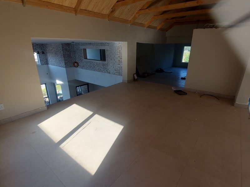 An expansive, unfinished open-plan loft area featuring exposed timber rafters, tiled flooring, and exposed brick accents, offering a versatile space for custom development.