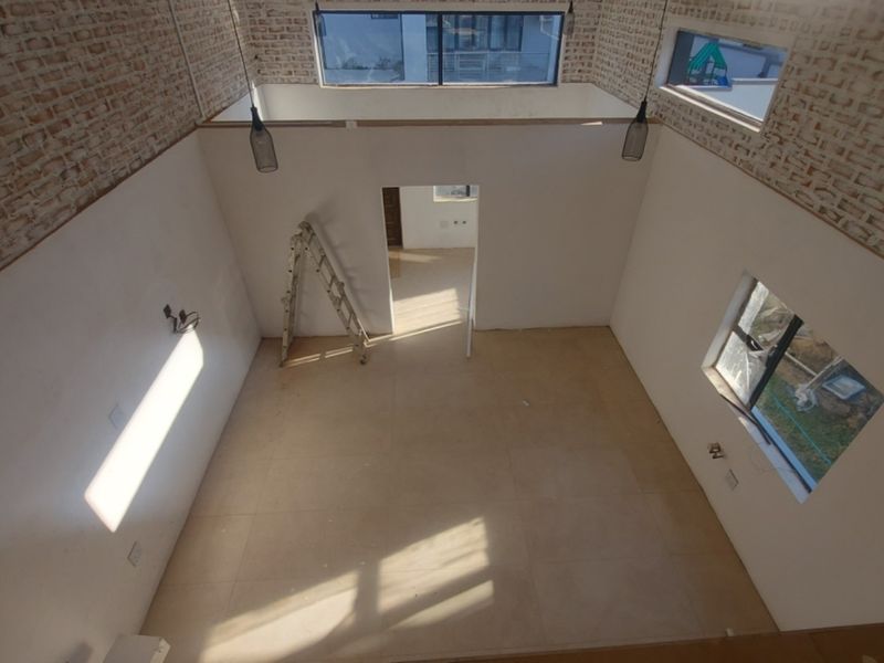 Spacious double-volume living area featuring exposed brick walls, large windows for natural light, and tiled flooring, currently in an unfinished state.