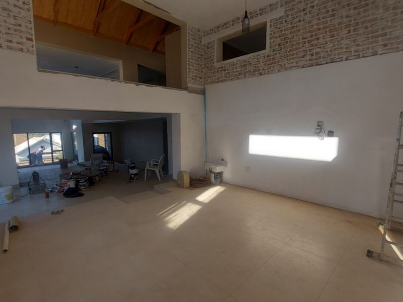 Spacious open-plan living area under construction, featuring high vaulted timber ceilings, exposed brick accents, and a mezzanine level with tiled flooring throughout.