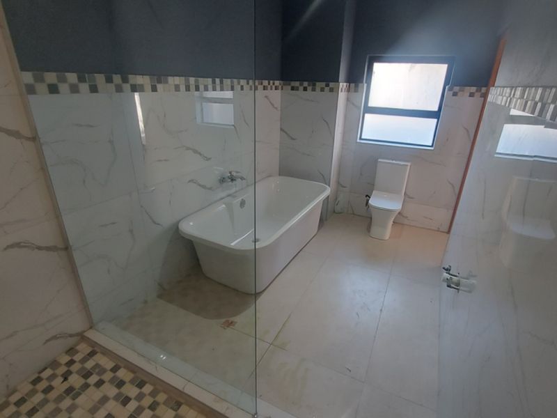 Modern bathroom featuring a freestanding bathtub, glass shower enclosure, and marble-look wall tiles with a decorative mosaic border.
