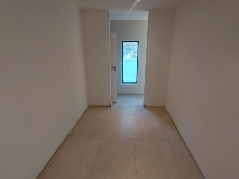A clean, empty hallway featuring neutral tiled flooring and a window providing natural light.