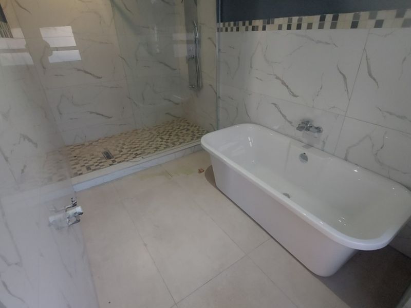 Modern bathroom featuring a freestanding bathtub, a spacious walk-in shower with glass enclosure, and elegant marble-look wall tiling.