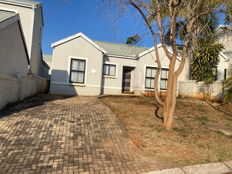 Front elevation of a single-story house featuring a paved driveway, security gate entrance, and a small front garden area.